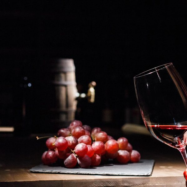 Woman holds glass of wine before bunch of grape lying on black plate